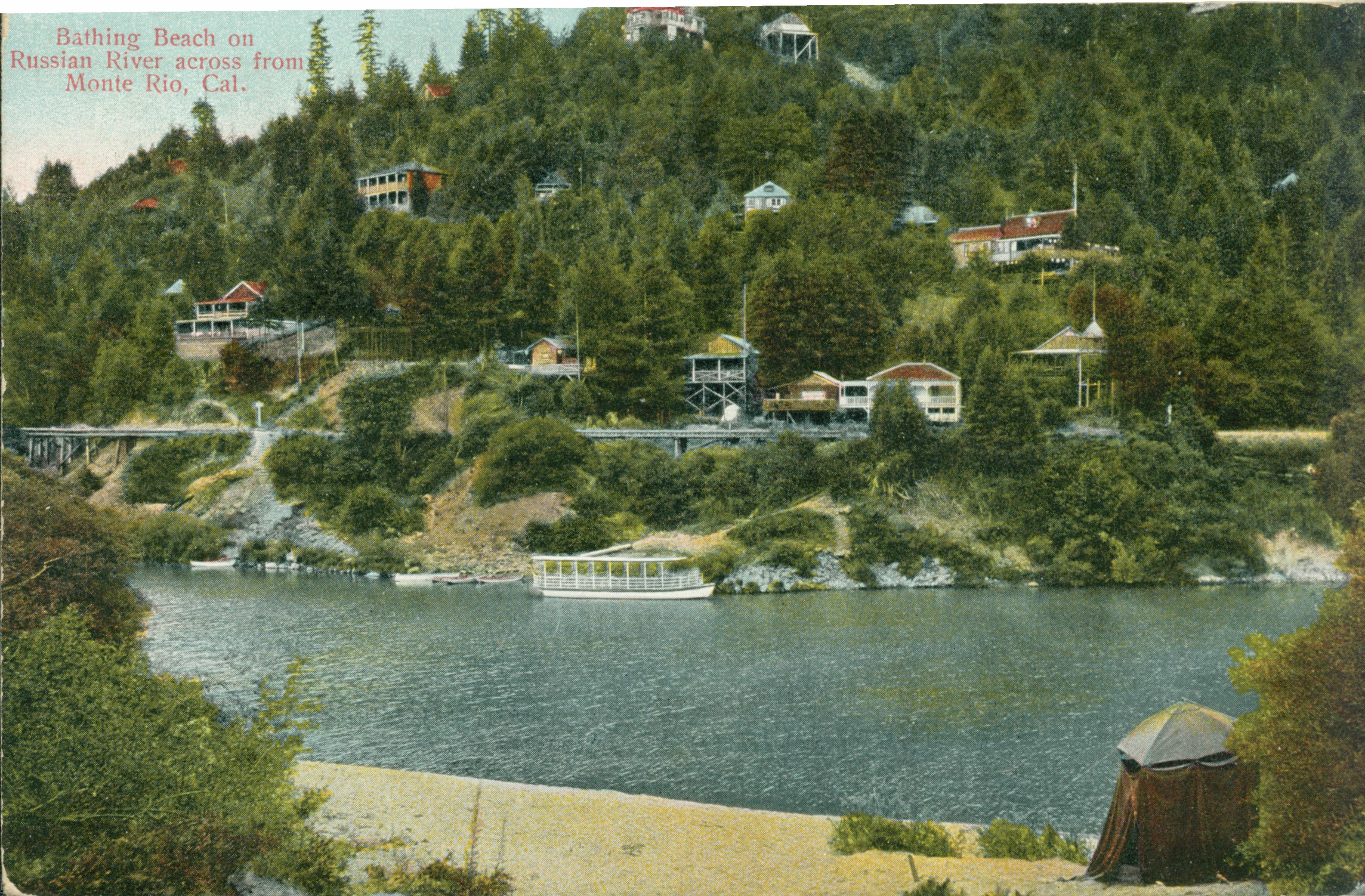 Shows a beach on the shores of the Russian River with Monte Rio's buildings and ferry on the other shore.